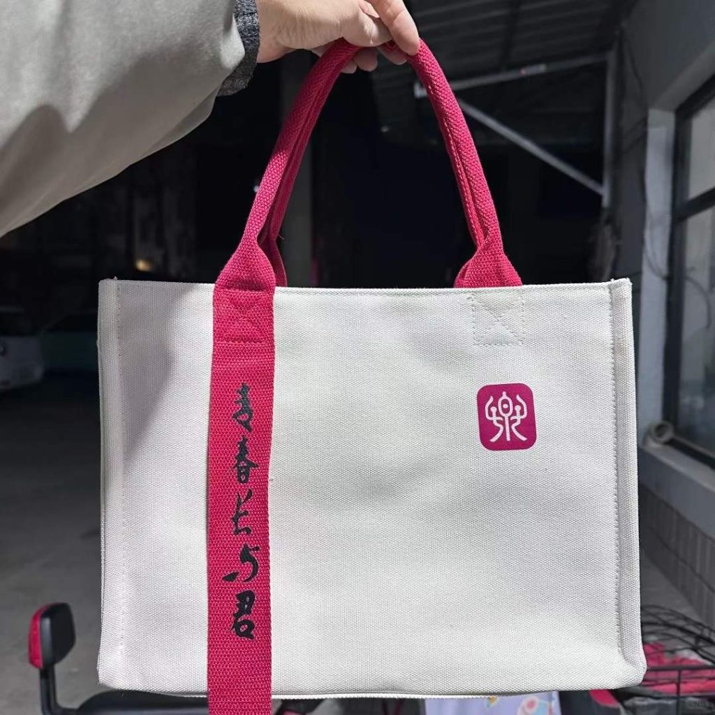 White triple-layer canvas tote bag with red webbing handles stitched down the front